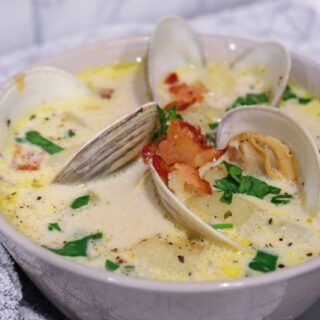 Close up picture of homemade New England Clam Chowder topped with fresh clams, bacon, and parsley.