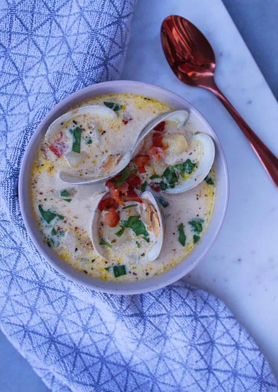 Overheat picture of Homemade New England Clam Chowder with fresh clams in a tan bowl wrapped in tea towel.