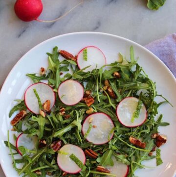 Radishes, pecans, mint, and arugula on a white plate over a marble countertop.