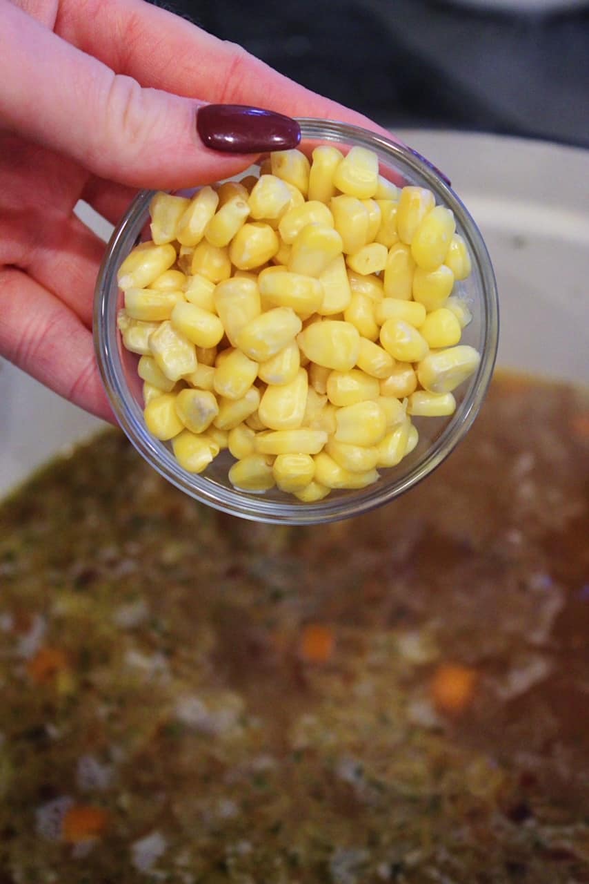 Adding corn in a bowl to homemade clam chowder in large dutch oven.