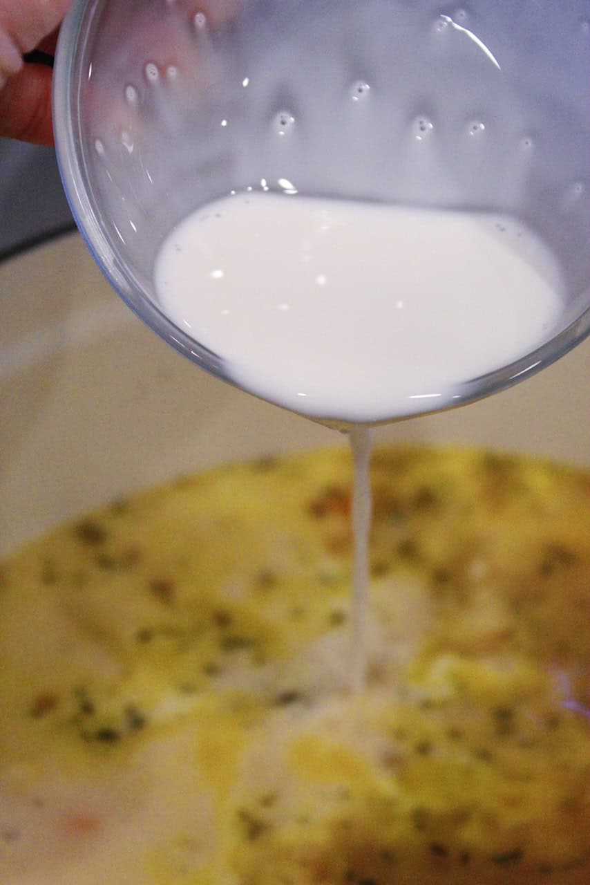 Pouring heavy cream into homemade clam chowder.