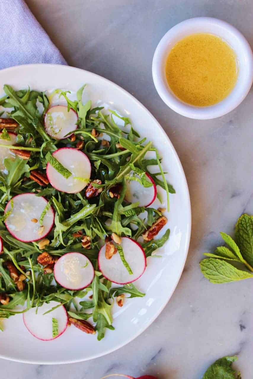 Radish Salad on white plate sitting next to a white cup of Honey Mustard Vinaigrette.