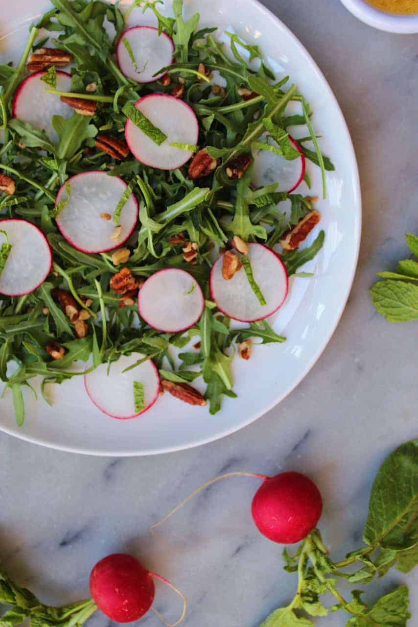 Radishes and pecans over a bed of arugula on a marble countertop. 