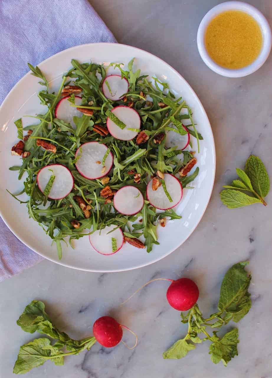 Radish Salad on white plate sitting next to a white cup of Honey Mustard Vinaigrette.