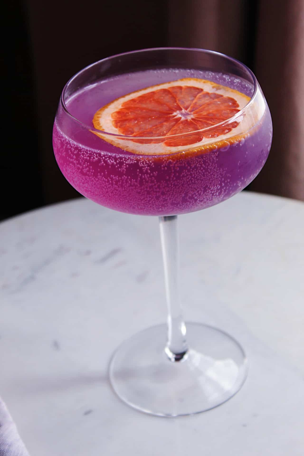 Pink/purple Grapefruit Gin Cocktail with grapefruit garnish in couple glass.