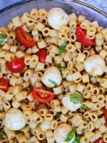 Caprese Pasta Salad with mozzarella balls, tomatoes, basil in a bowl.