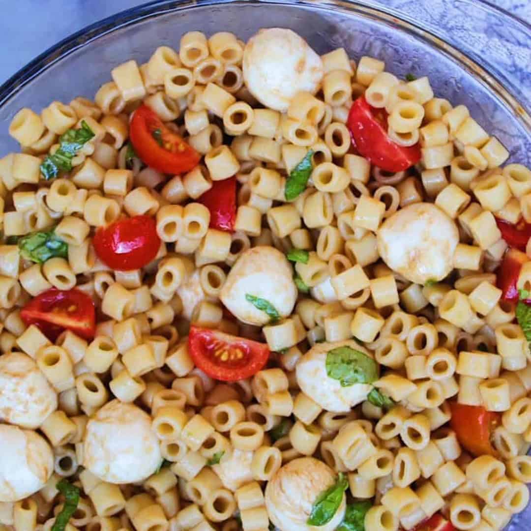 Caprese Pasta Salad with mozzarella balls, tomatoes, basil in a bowl.