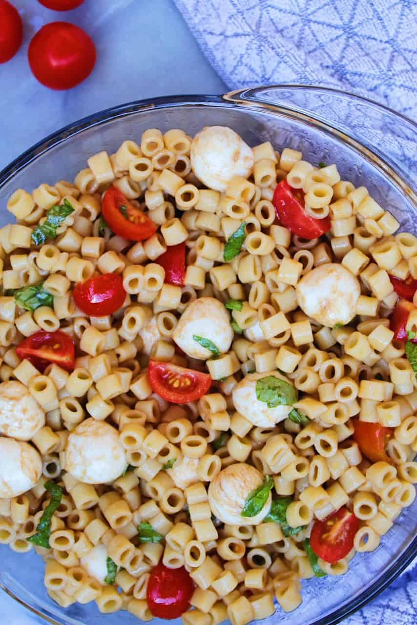 Caprese Pasta salad with tomatoes, mozzarella balls, basil in a clear bowl.