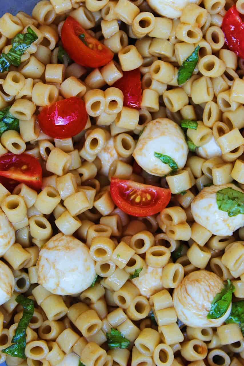 Close up of balsamic dressing drizzled over noodles, mozzarella, and tomatoes.