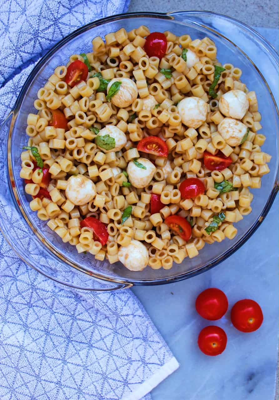 Caprese Pasta Salad in a clear bowl on a marble counter.