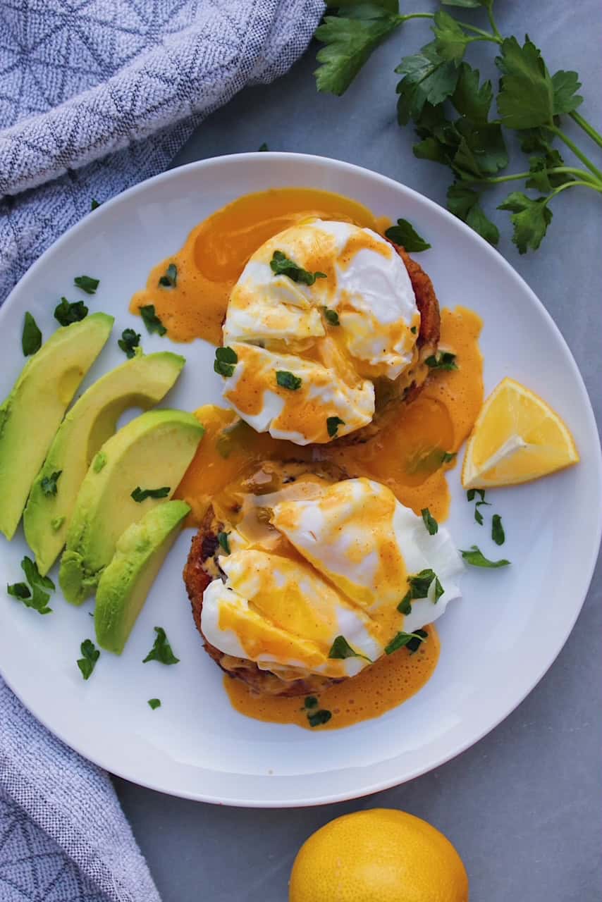 Overhead shot of Crab Cakes Eggs Benedict on a white plate with avocado.