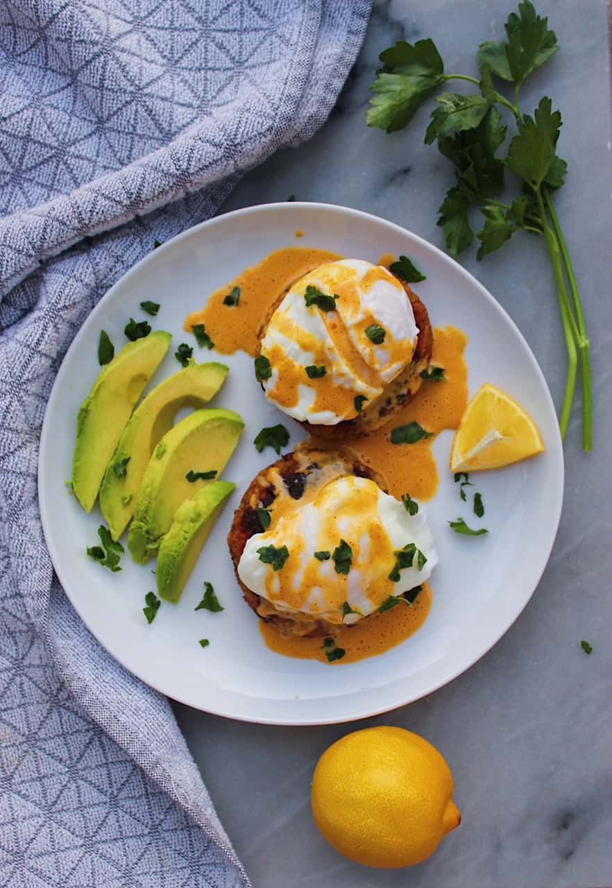 Overhead shot of Crab Cakes Benedict on white plate with lemon and avocado.