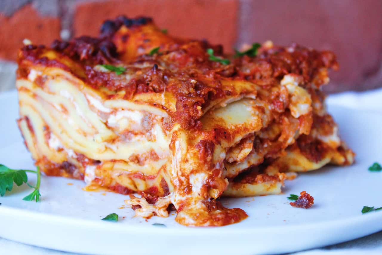 Slice of lasagna with melted cheese on a white plate.