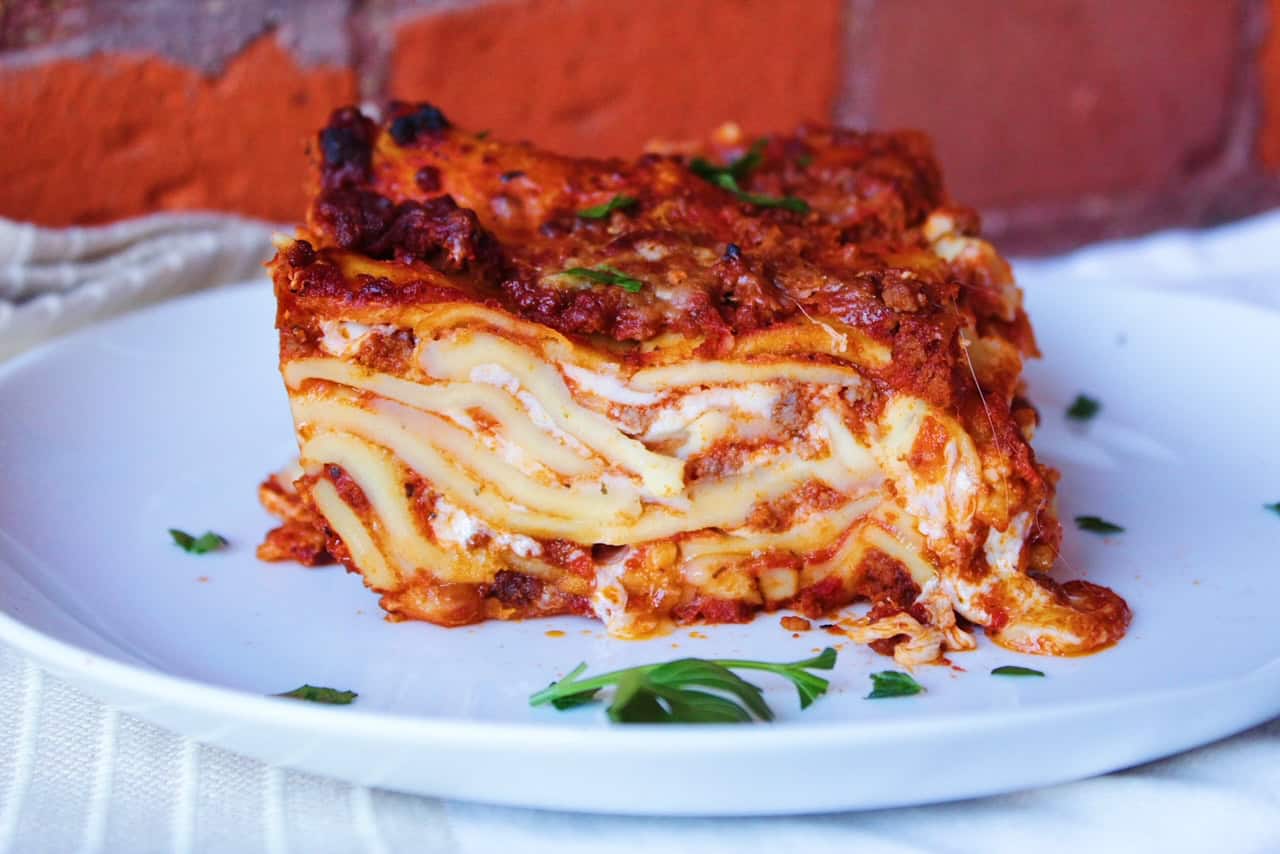 A slice of lasagna from scratch on a white plate with parsley.