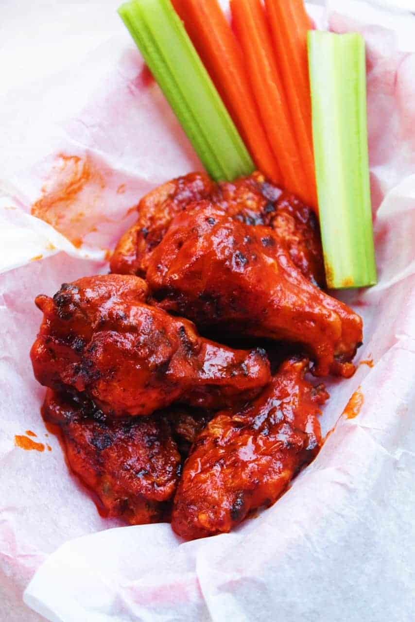 Crispy Air Fryer Hot Wings in a parchment paper lined basket with celery and carrots.