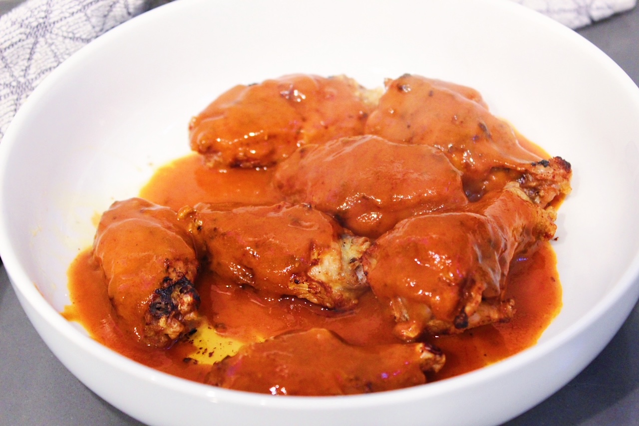 Air fried chicken wings being tossed in spicy buffalo hot sauce in a white bowl.
