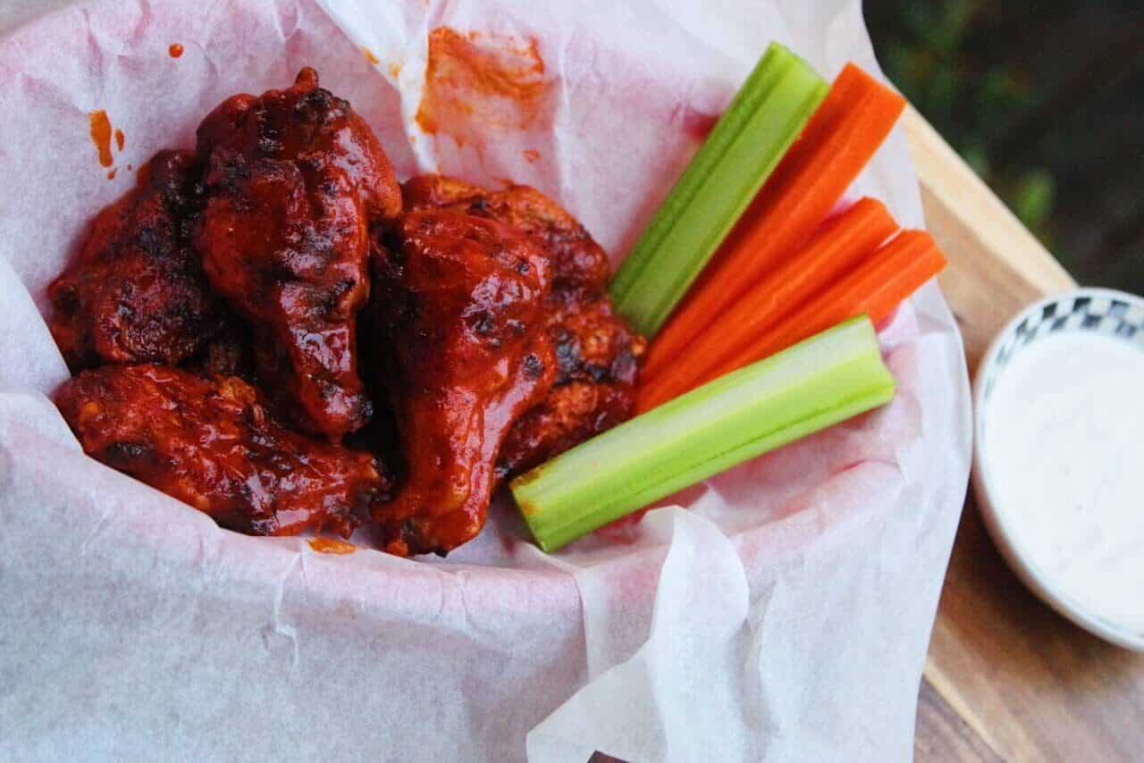 Side view of Crispy Air Fryer Hot Wings in a parchment paper lined basket with ranch, celery and carrots.