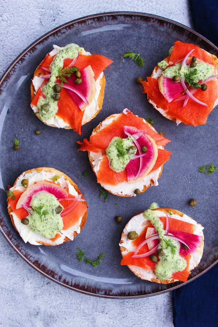 Five mini bagels with lox on a grey plate.