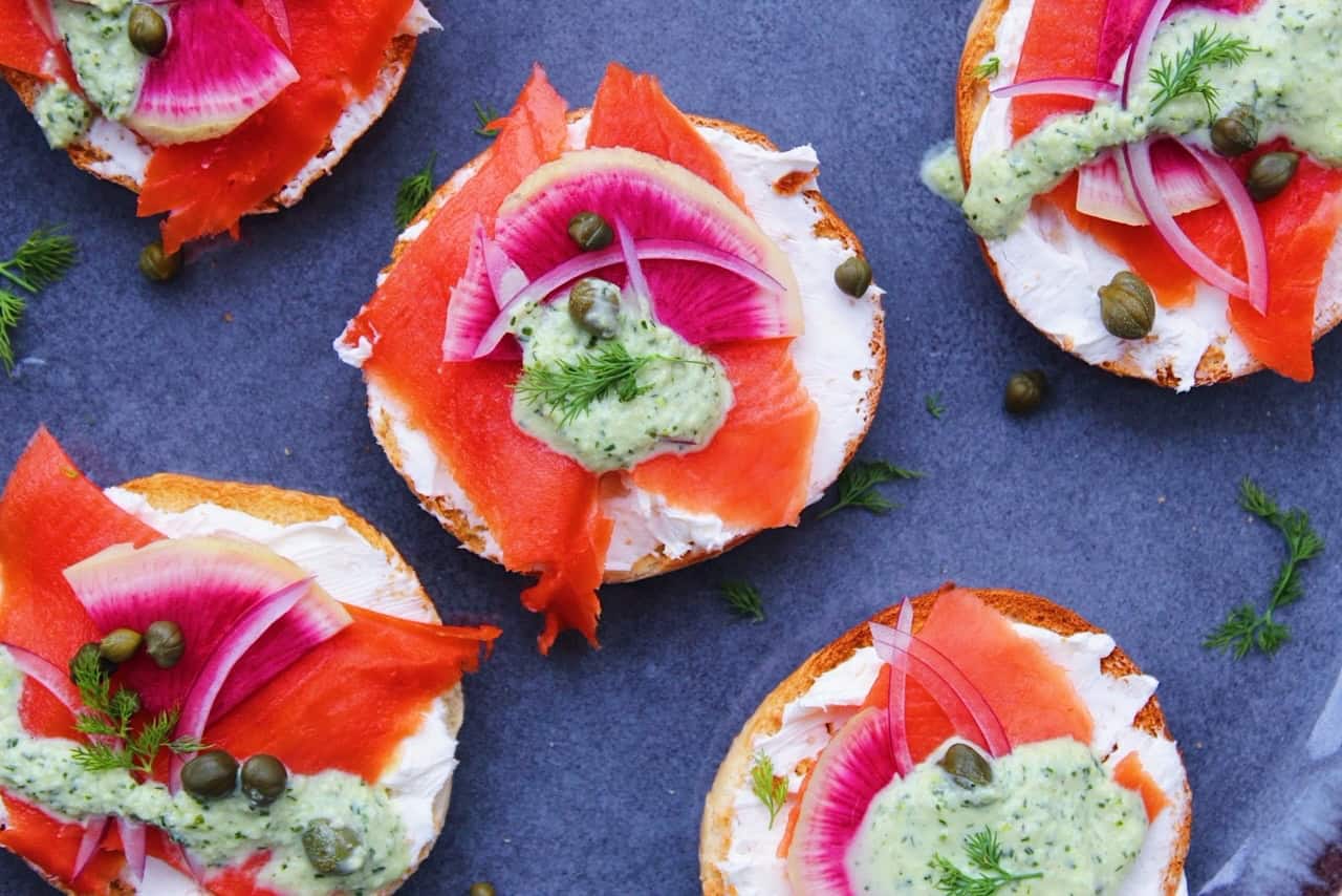 Overhead image of mini bagels topped with salmon, cream cheese, and more on a plate.