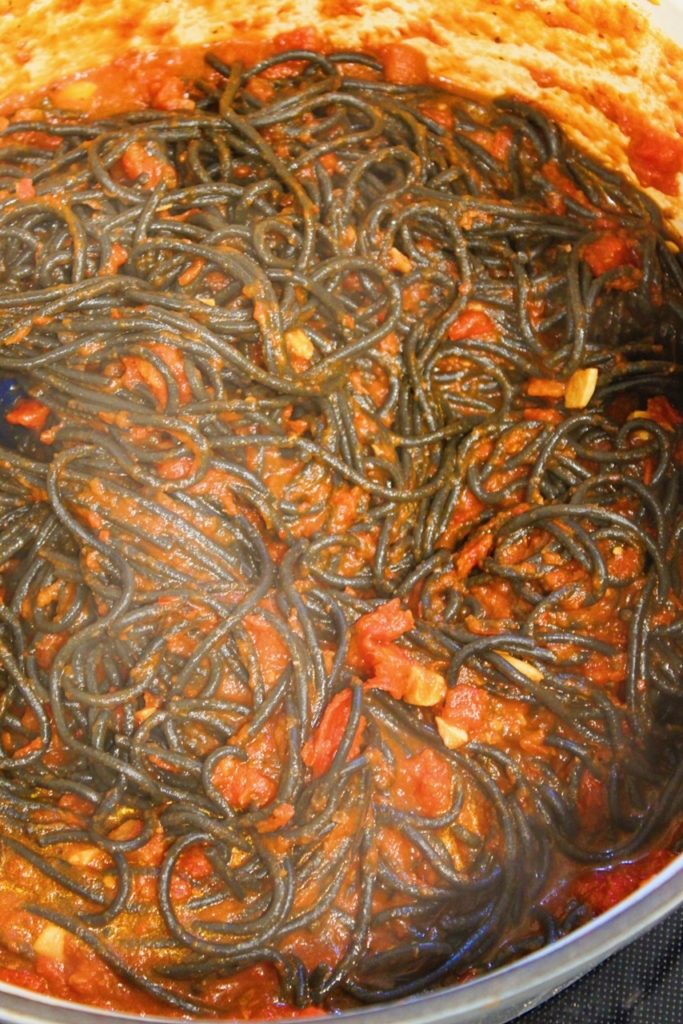 Picture of mixing cooked and drained squid ink noodles with arrabbiata sauce.
