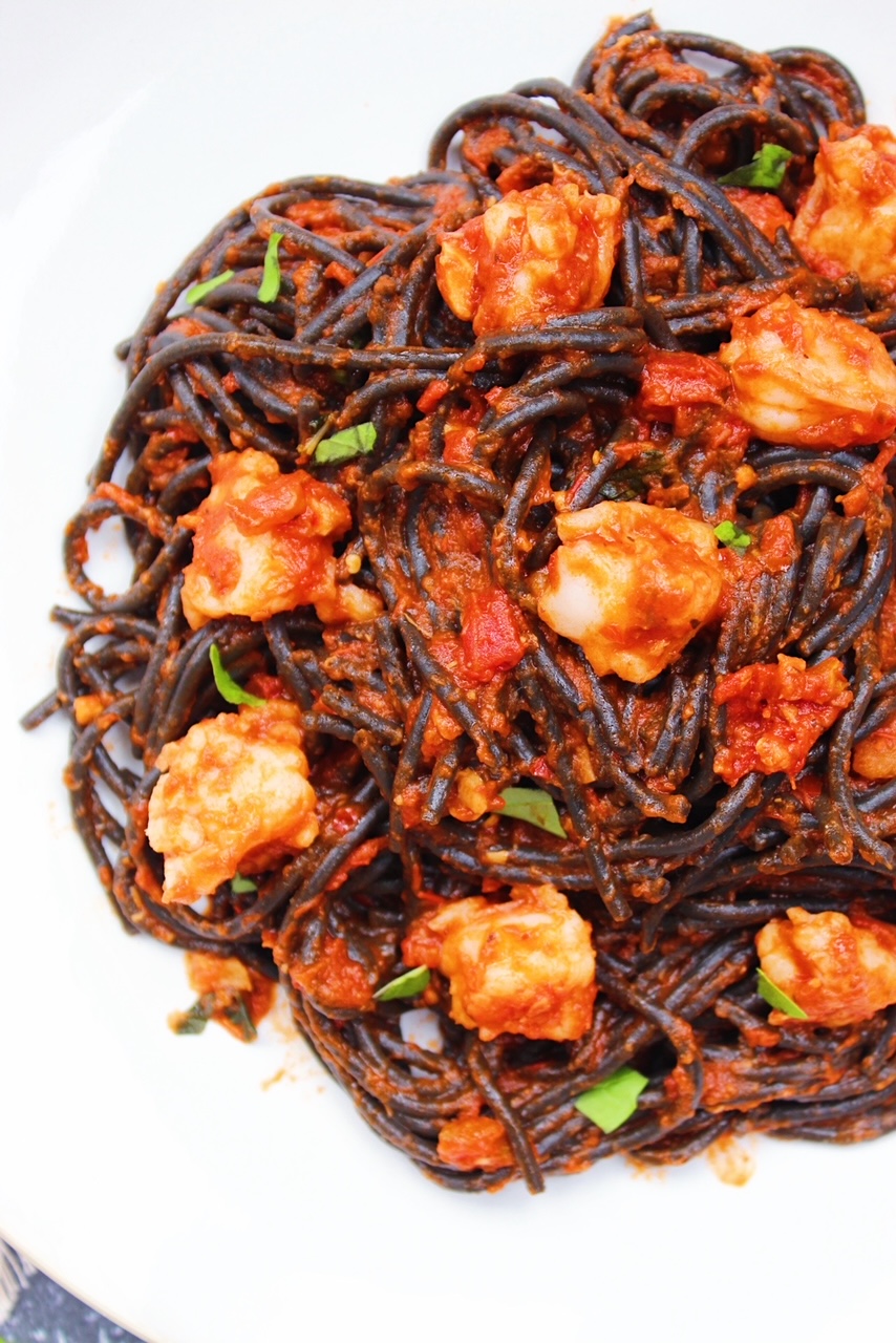 Close up picture of squid ink noodles mixed with sauce and shrimp on white plate.