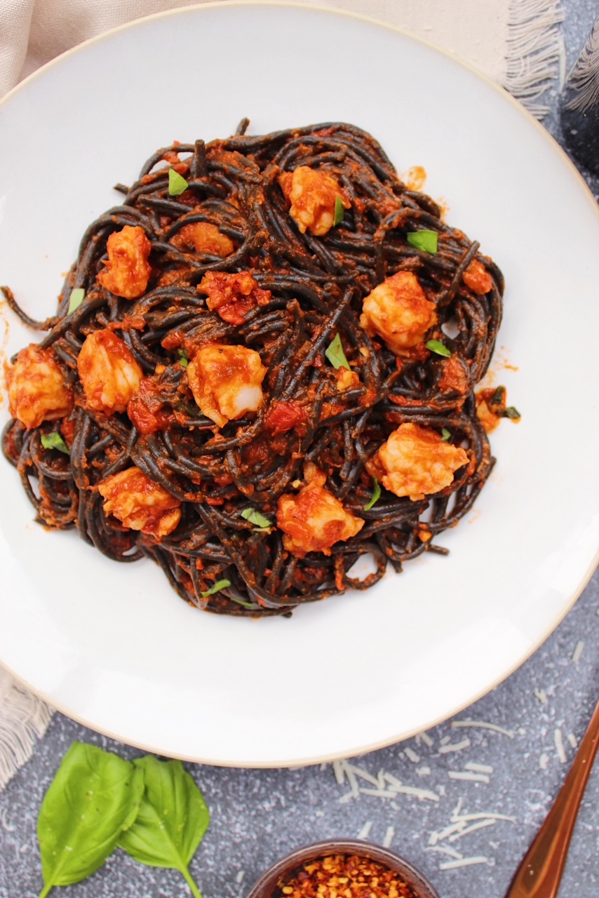 Overhead picture of squid ink pasta topped with shrimp and basil.