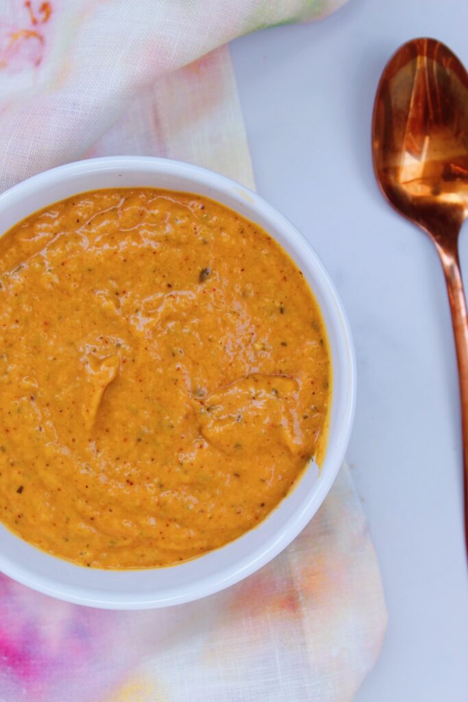 A tanish-orange colored creamy burger sauce in a bowl with a rose gold spoon laying next to it.