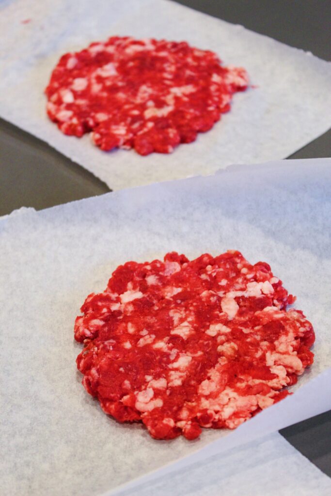 Two smashed burger patties on parchment paper.