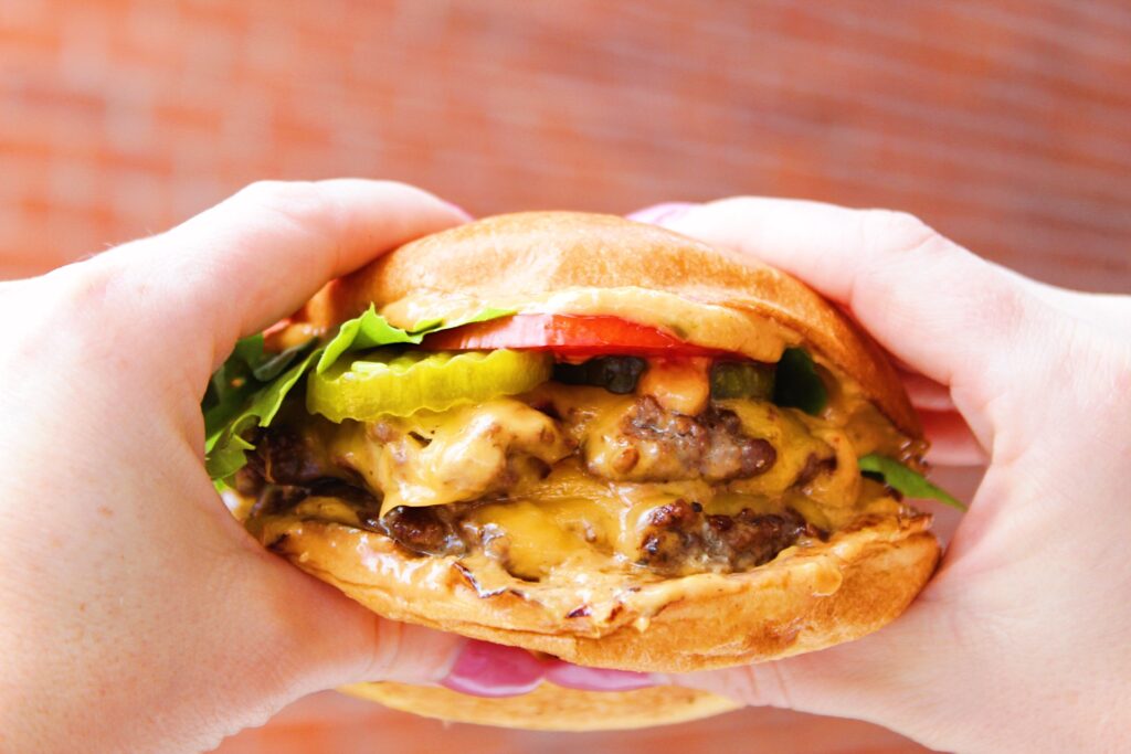 Two hands squashing a juicy smash burger.