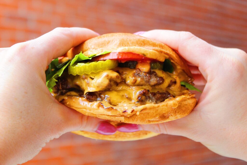 Close up of two hands holding a delicious smash burger.