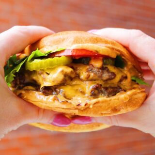 Close up of two hands holding a delicious smash burger.