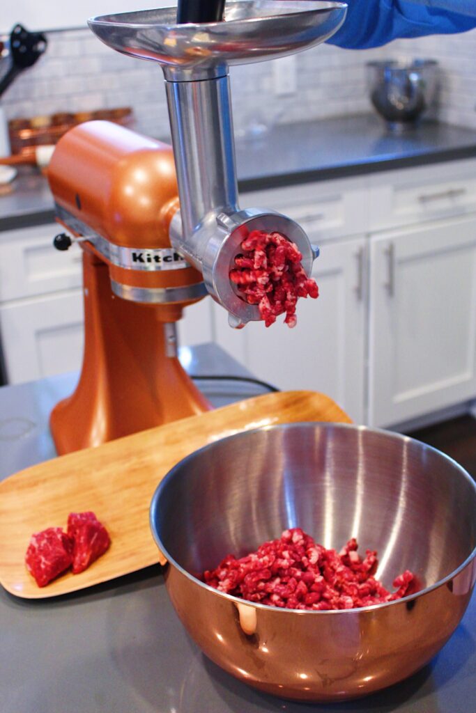 Pushing short rib poritons through meat grinder to make ground beef.