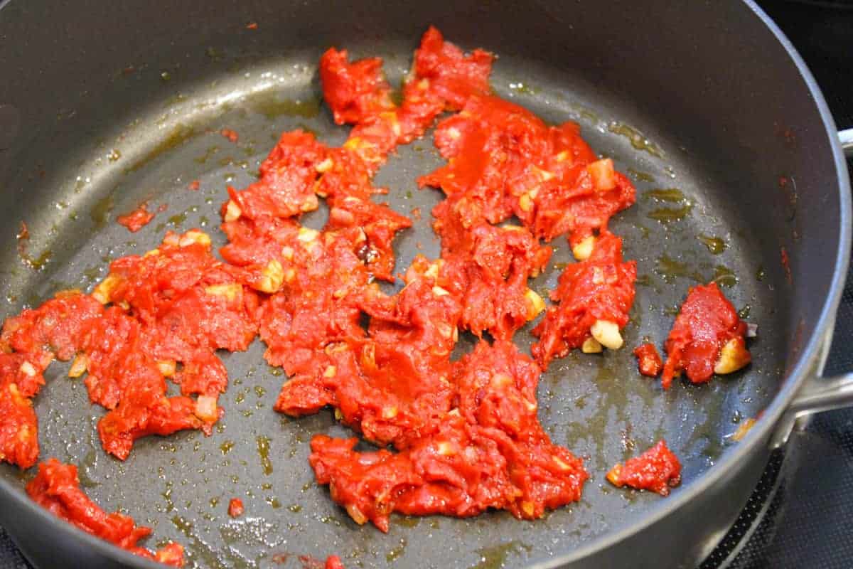 Tomato paste and fresh garlic sauteing in a pan.