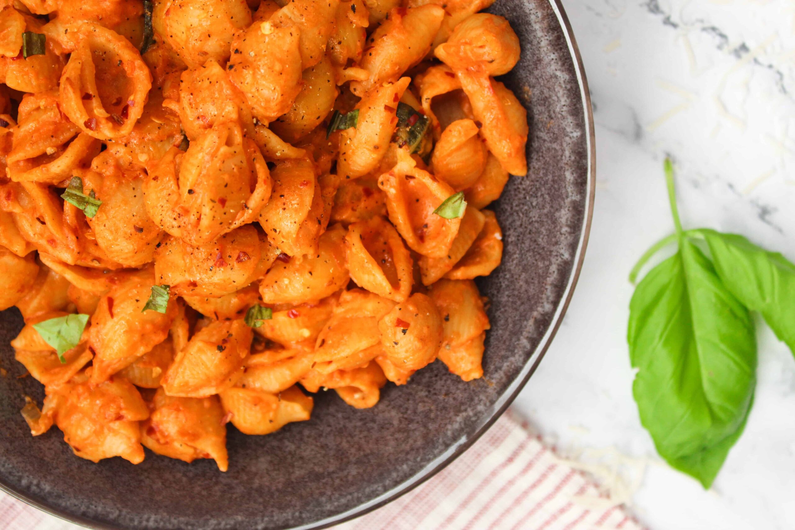 Close up of Gigi Hadid Pasta (Spicy Vodka Sauce Shells) with fresh basil in a bowl on a dish towel.