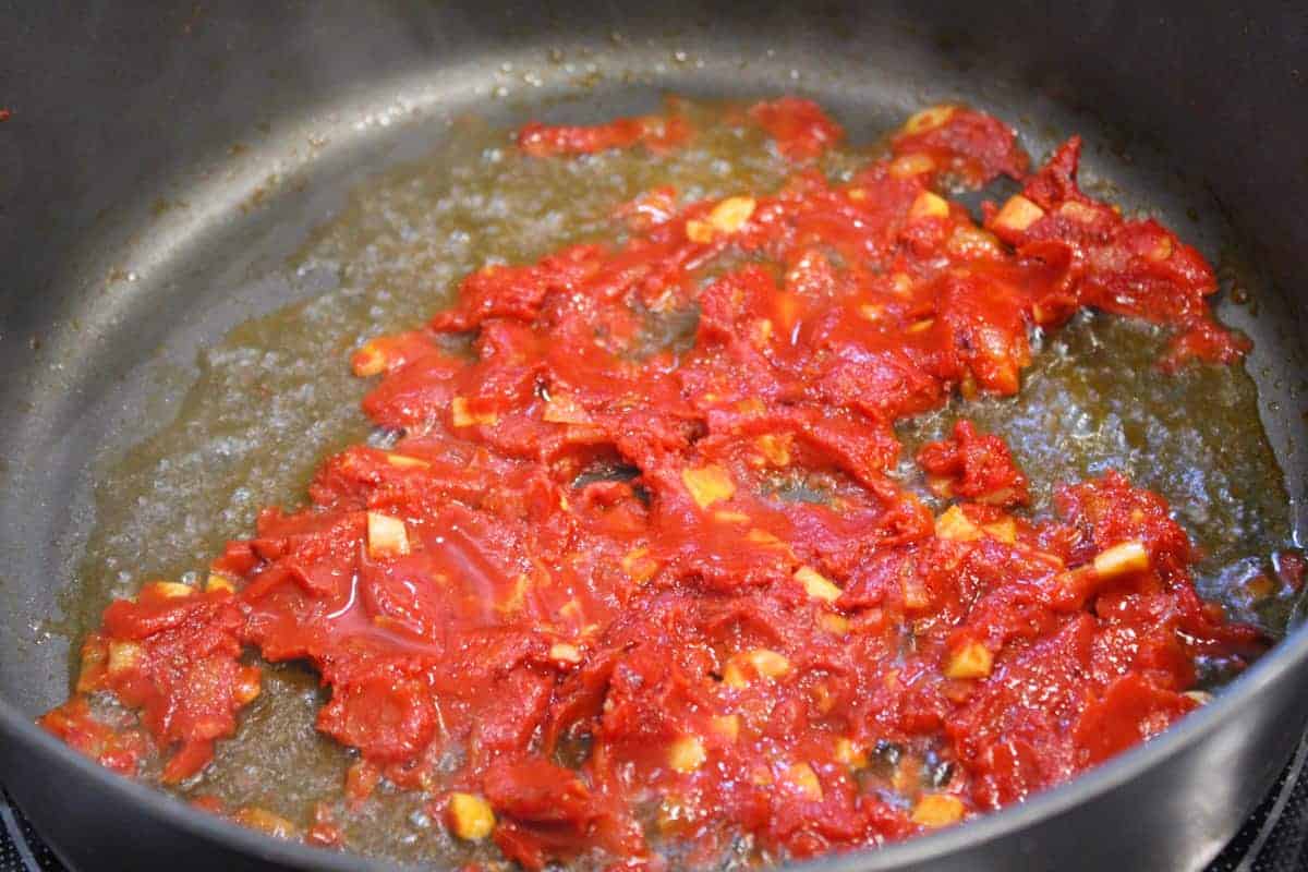 Tomato paste and fresh garlic being cooked with vodka to form vodka sauce.