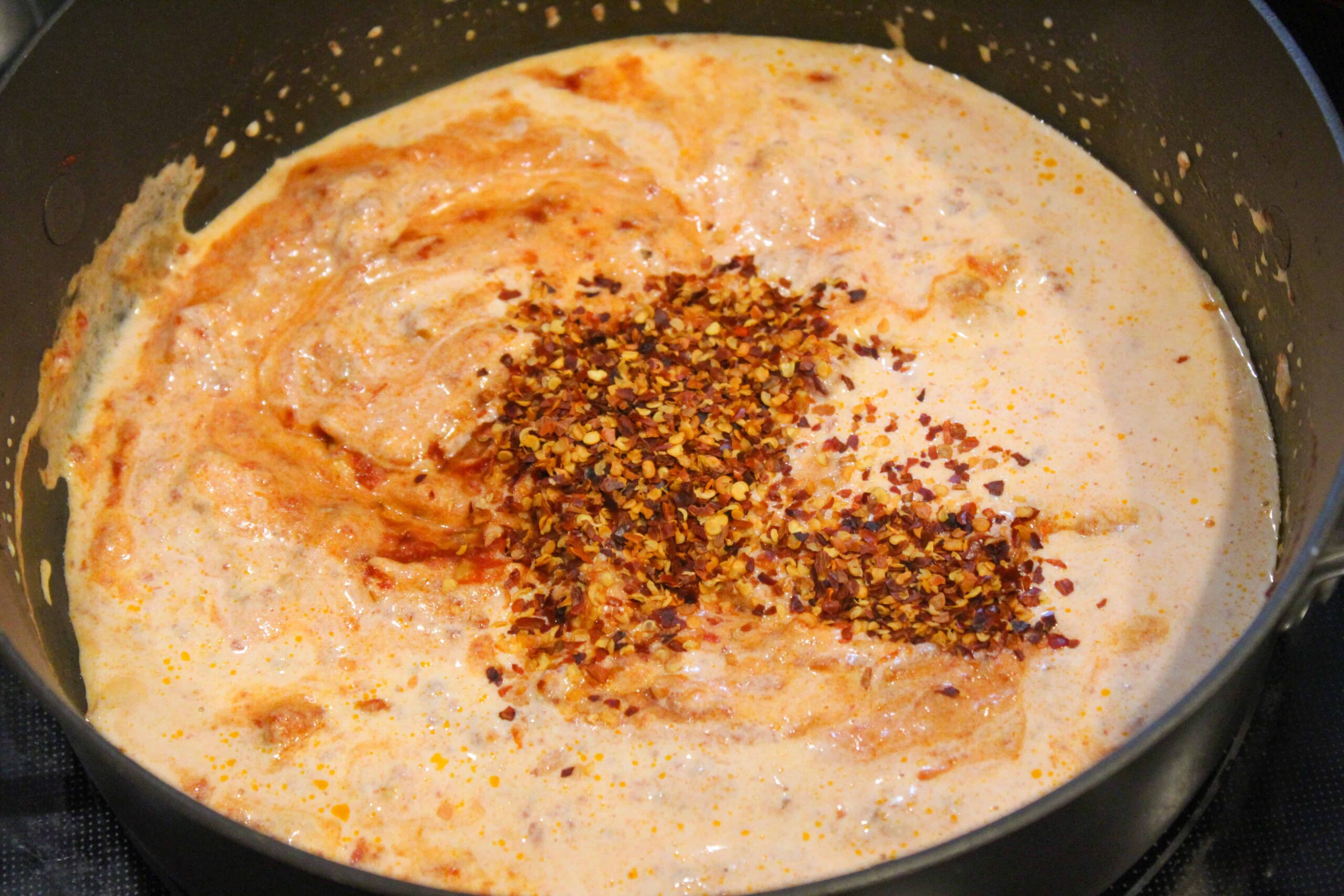 Adding red pepper flakes to spicy vodka sauce in black sauce pan.