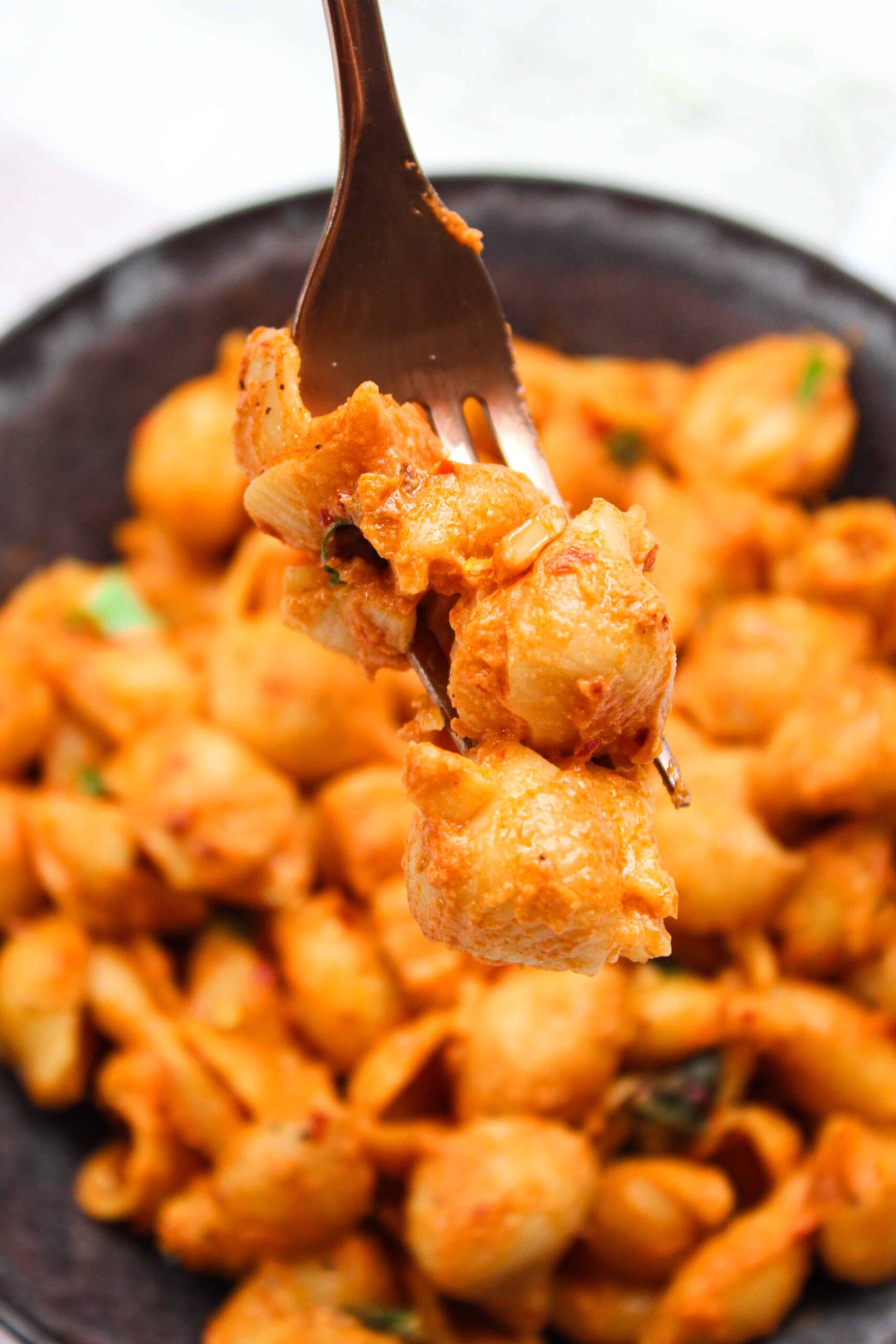 A fork with spicy vodka sauce shells and fresh basil.