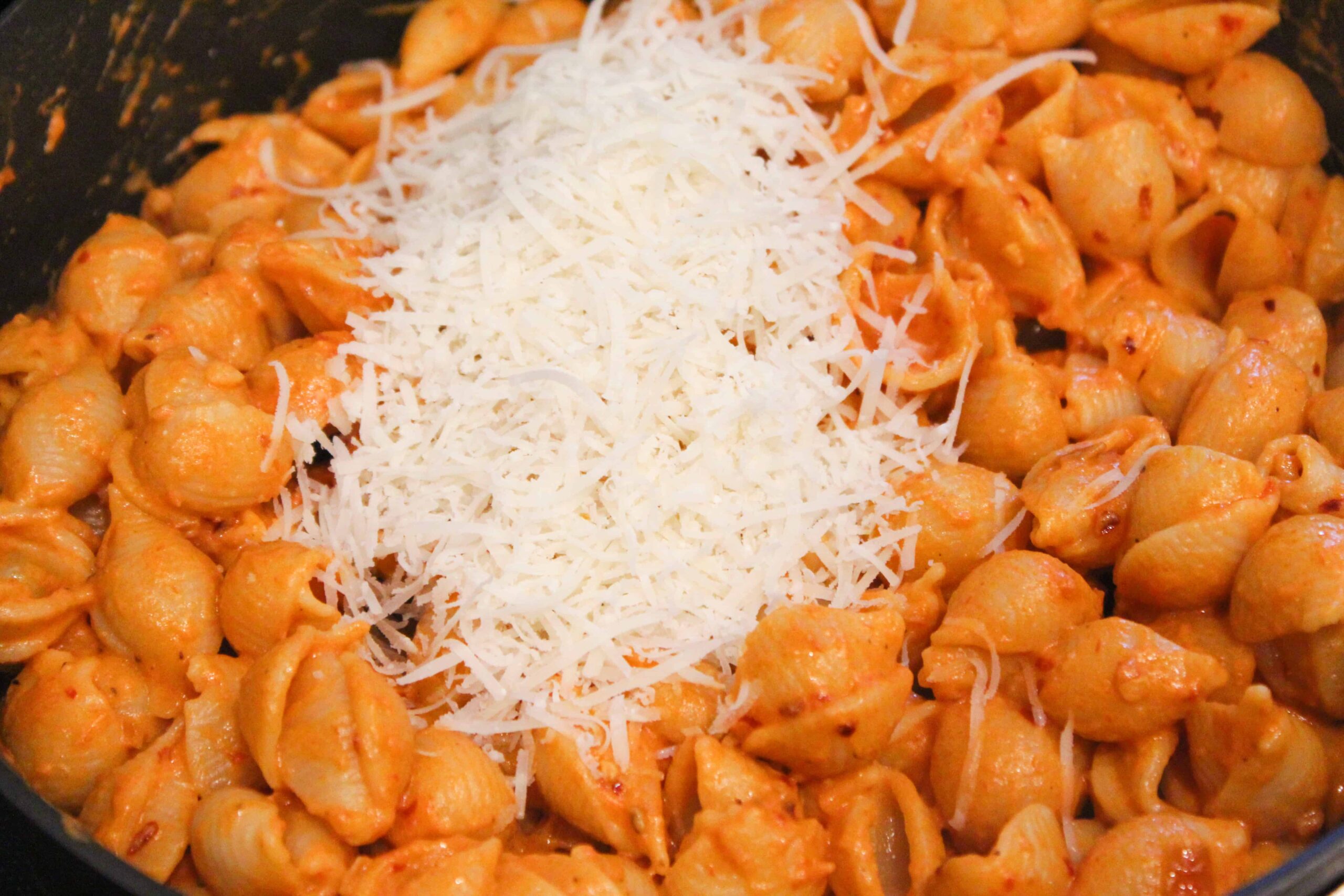 Heap of fresh Parmesan being added to spicy vodka sauce shells.