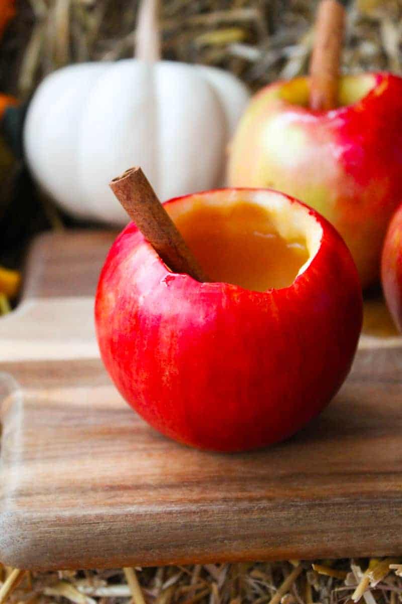 A red apple containing apple cider cocktail and a cinnamon stick next to a pumpkin.