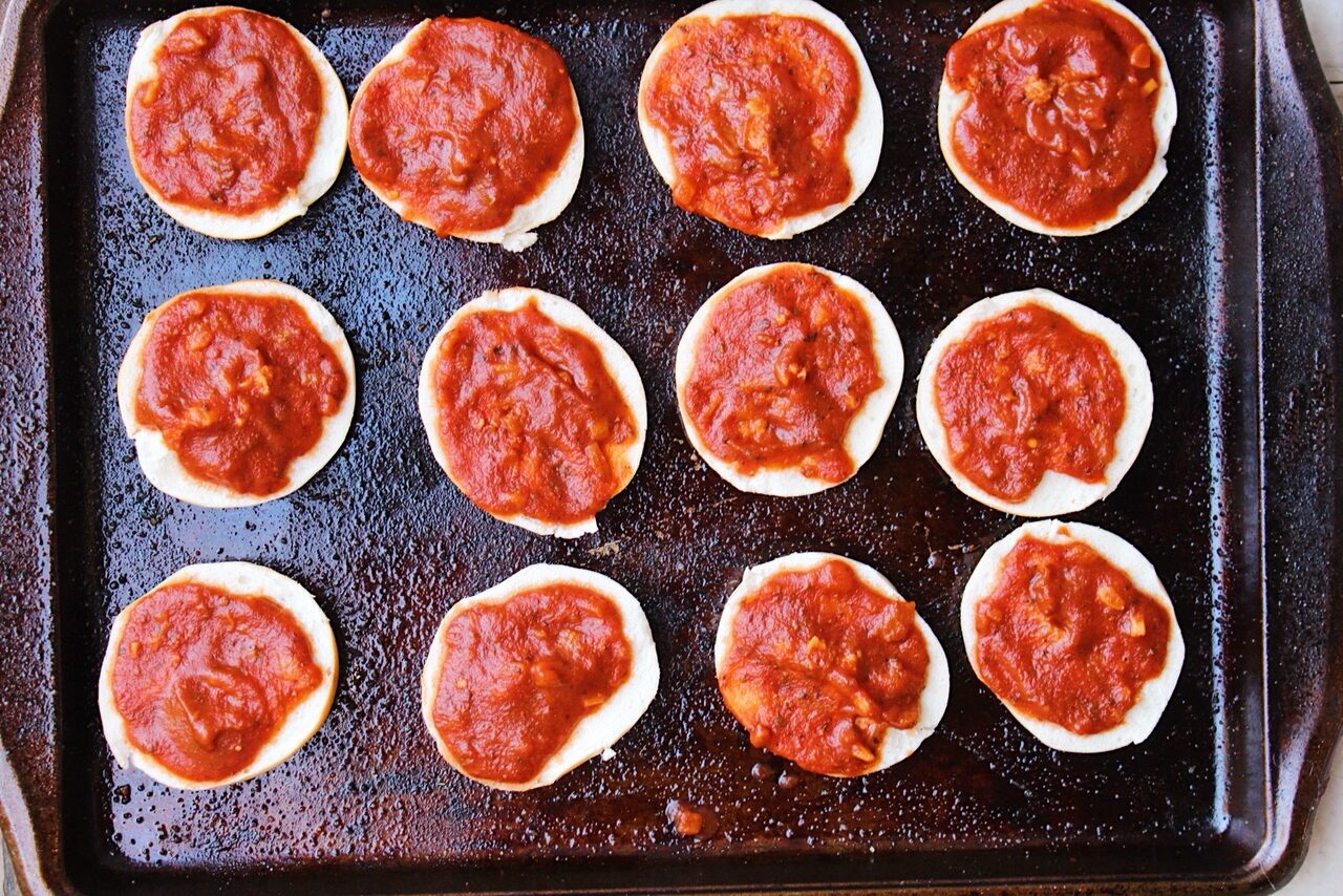 Mini bagels topped with homemade marinara sauce on a baking sheet.