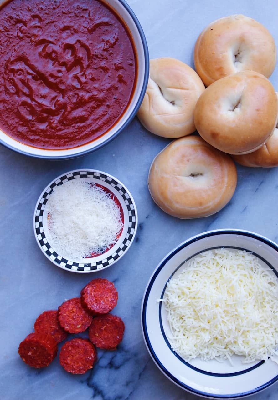 Overhead shot of pizza bagel ingredients including marinara, mini bagels, fresh parmesan, pepperoni and mozzarella.