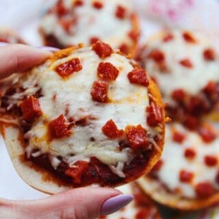 Close up picture holding a mini homemade pizza bagel bite topped with melted mozzarella and pepperoni.