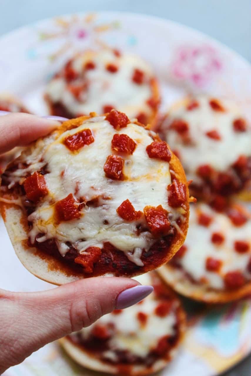 Close up picture holding a mini homemade pizza bagel bite topped with melted mozzarella and pepperoni.