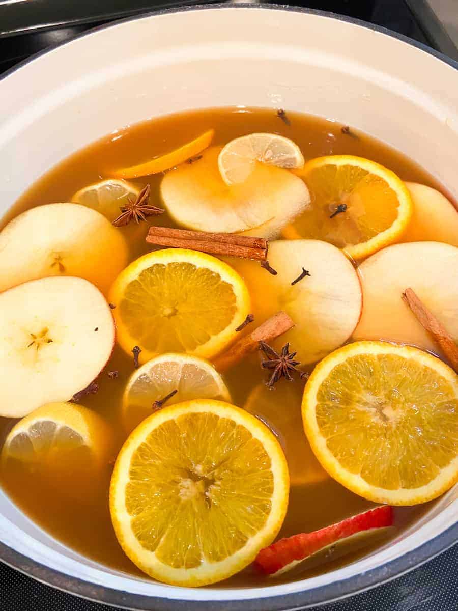 Apple cider simmering with spices, apple, orange, and lemon slices in large dutch oven.