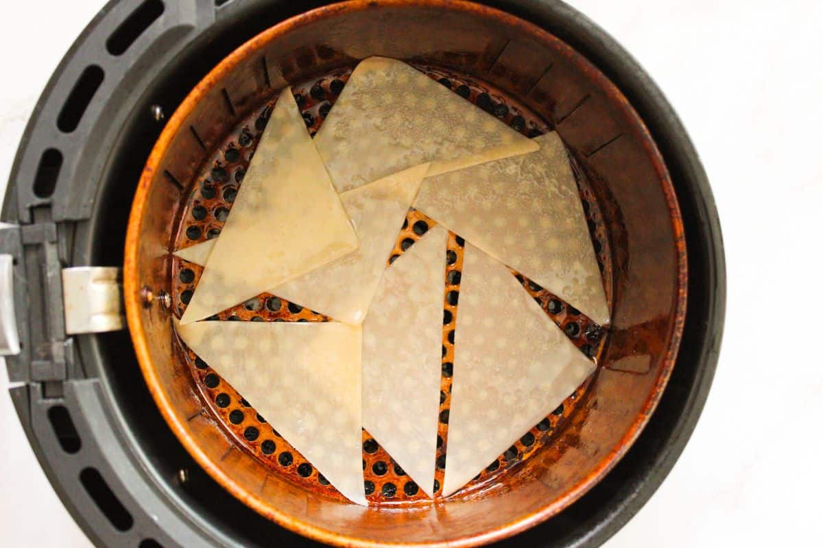 Wonton wrappers cut in triangles laid out in the basket of an air fryer.