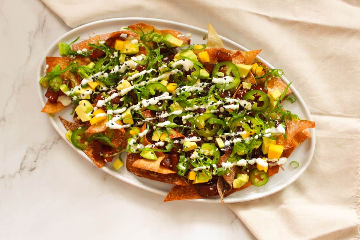 Overhead image of Ahi Tuna Nachos loaded with toppings on a white plate next to linen towel. 