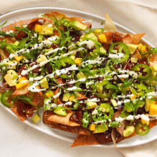 Overhead shot of Spicy Ahi Tuna Poke Nachos loaded with avocado, seaweed salad, and jalapenos on a white plate.