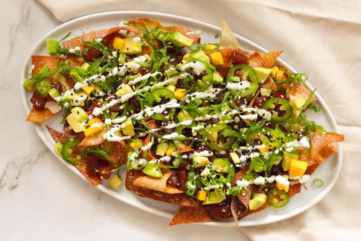 Overhead shot of Spicy Ahi Tuna Poke Nachos loaded with avocado, seaweed salad, and jalapenos on a white plate.