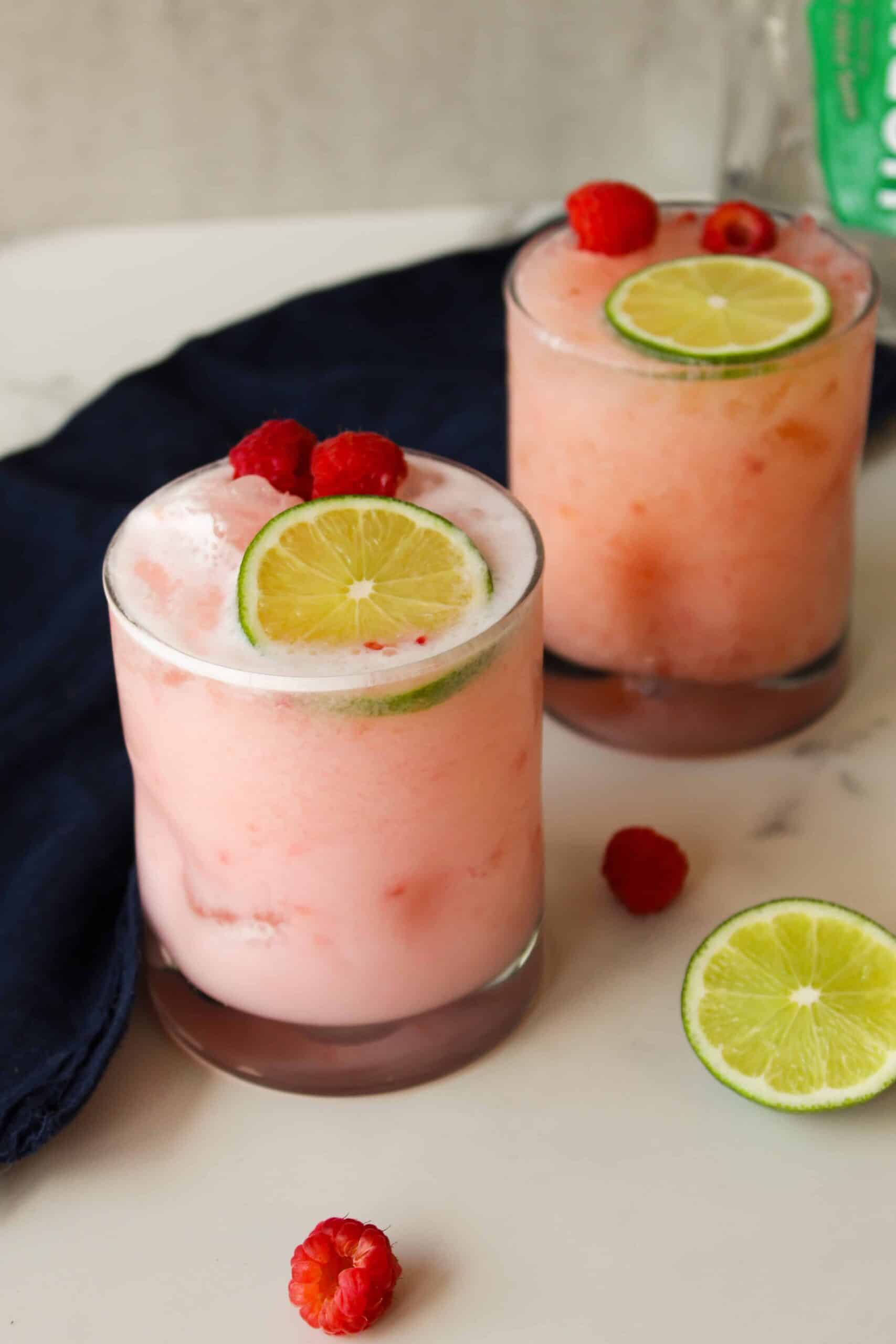 Two pale pink raspberry coconut margaritas with a blue tea towel.