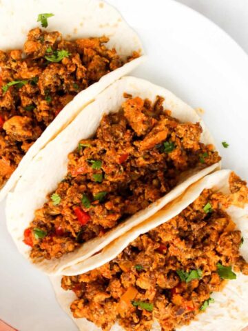 Overhead image of Chorizo Breakfast tacos in tortillas on a white plate.